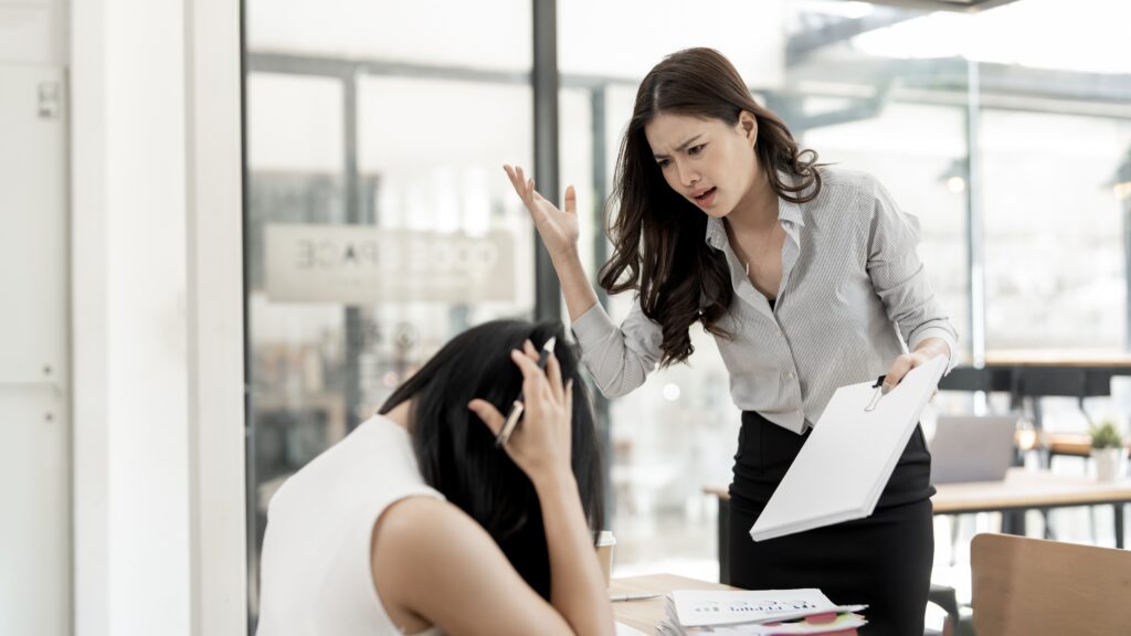 Female manager angrily confronting a stressed employee during a tense workplace conflict